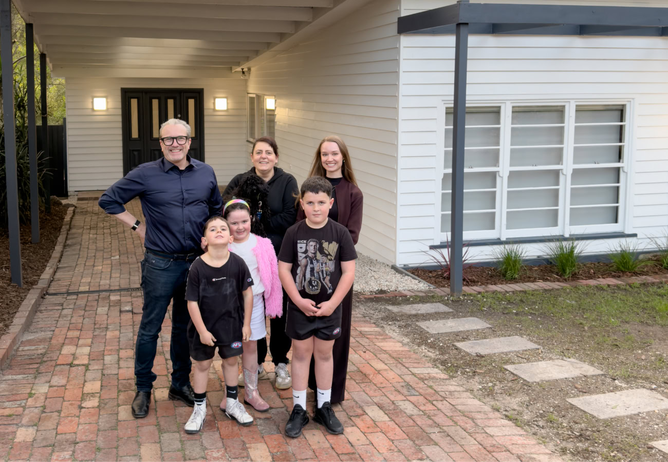 St Ferrer Impact Build 2026 Recipient, Angelina and family standing in front of renovated house